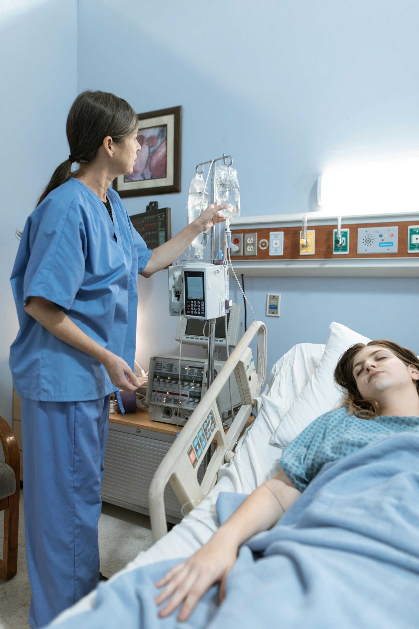 A nurse attends to a patient in a hospital room, ensuring medical equipment is functioning.
