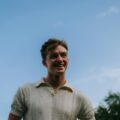 Casual portrait of a smiling young man under a blue sky, capturing summer joy.